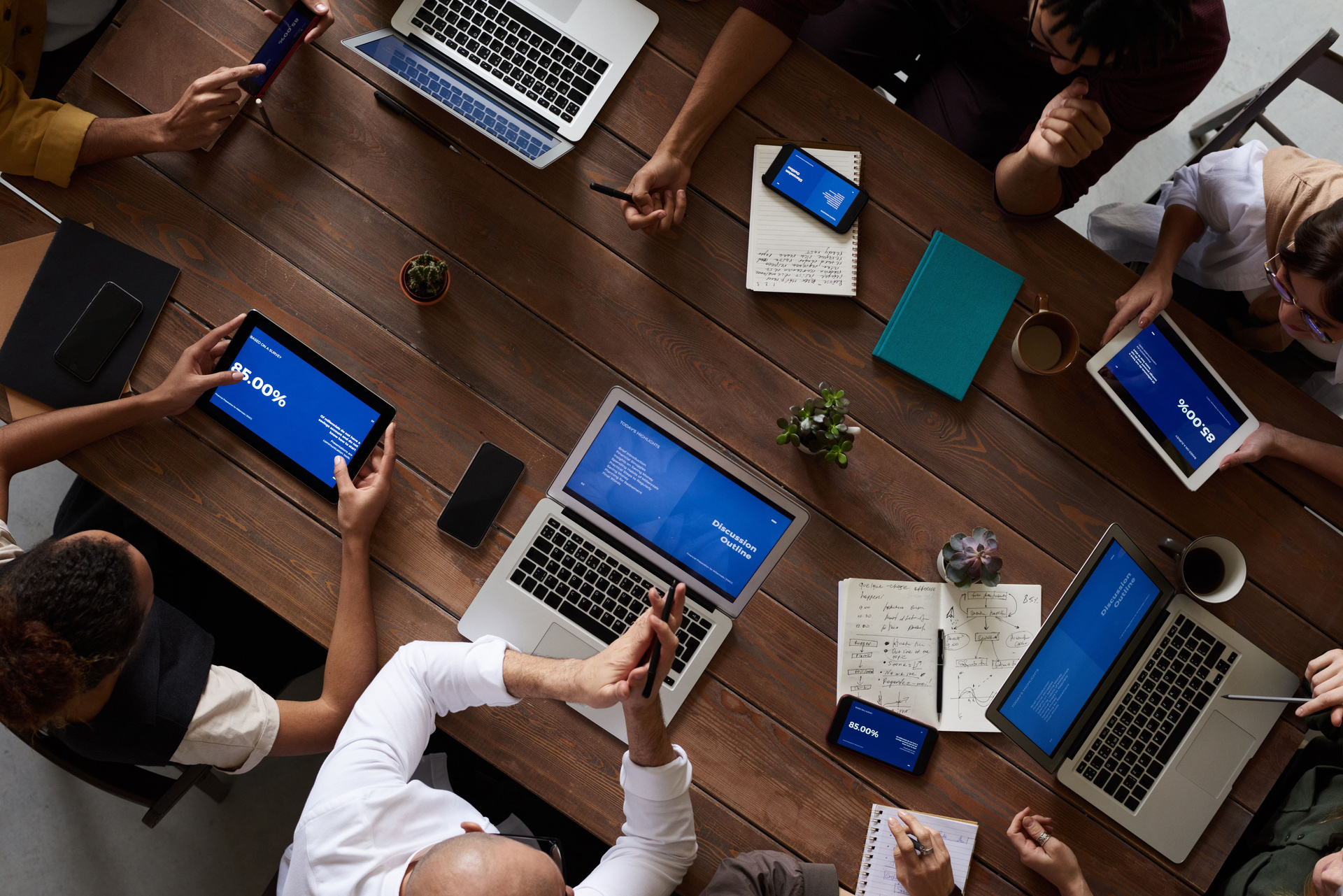 Overhead view of a discussion around a table, with notebooks, laptops, and tablets